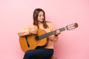 İzole edilmiş pembe arka planda gitar çalan esmer bir kız.
