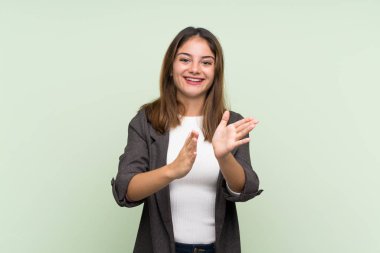 Spor ceketli genç esmer kız, izole edilmiş yeşil arka planda bir konferanstan sonra alkışlıyor.