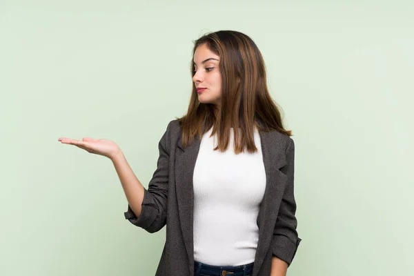 Joven Morena Con Chaqueta Sobre Fondo Verde Aislado Sosteniendo Copyspace —  Fotos de Stock