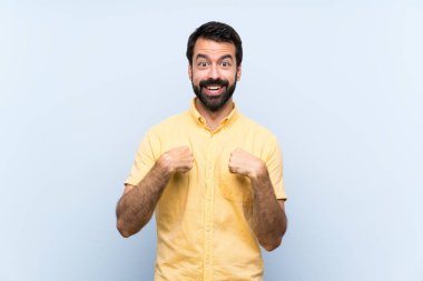 Sakallı genç bir adam izole edilmiş mavi bir geçmişi var ve yüzünde sürpriz bir ifade var.