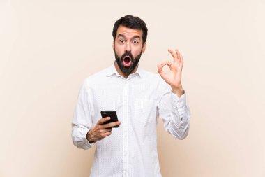 Elinde cep telefonu olan sakallı genç adam şaşırmış ve işaret veriyor.