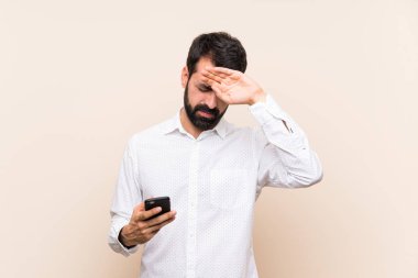 Sakallı genç adam elinde yorgun ve hasta bir yüz ifadesi olan bir cep telefonu tutuyor.