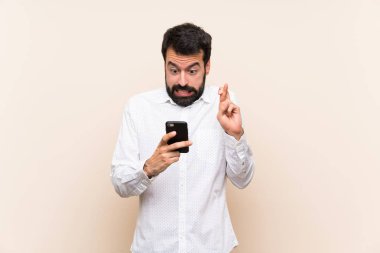 Sakallı genç adam parmakları çapraz bir cep telefonu tutuyor ve en iyisini diliyor.