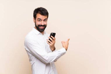 Sakallı genç adam elinde cep telefonu var.