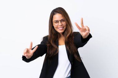 İzole edilmiş beyaz arka planda ceketi olan genç Brezilyalı kız gülümsüyor ve zafer işareti gösteriyor.