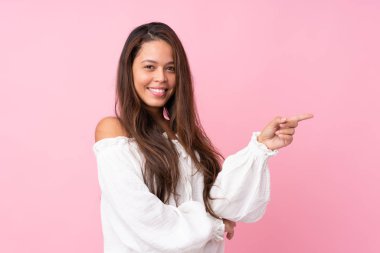 İzole edilmiş pembe arka planda genç Brezilyalı kız, parmağıyla kenarı gösteriyor.