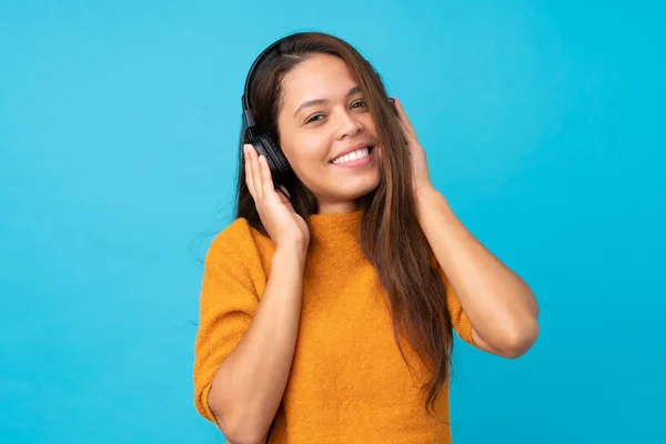 Mujer joven escuchando música sobre una pared azul aislada —  Fotos de Stock