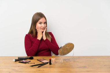 Sürpriz yüz ifadesi ile bir masada makyaj paleti ve kozmetik ile Genç kız