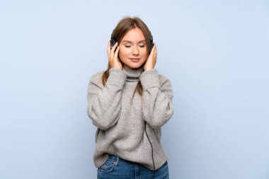 Izole mavi arka plan üzerinde kazak ile genç kız kulaklık ile müzik dinlerken