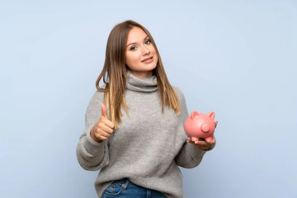 Teenagerka Svetrem Přes Izolované Modré Pozadí Velkým Piggytem — Stock fotografie