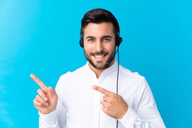 Tele-pazarlamacı adam kulaklıkla çalışıyor. İzole edilmiş mavi arka plan üzerinde.