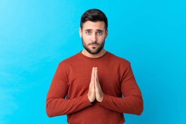 Sakallı, mavi arka planda genç yakışıklı adam yalvarıyor.