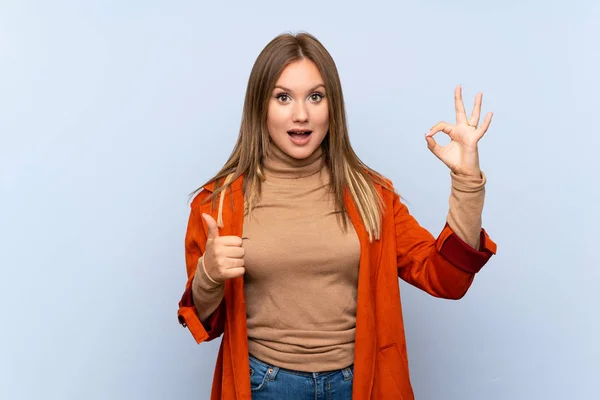 Menina Adolescente Com Casaco Sobre Fundo Azul Isolado Mostrando Sinal — Fotografia de Stock