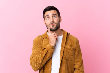Pembe arka planda kadife ceket giyen sakallı yakışıklı genç bir adam bir fikir düşünüyor.