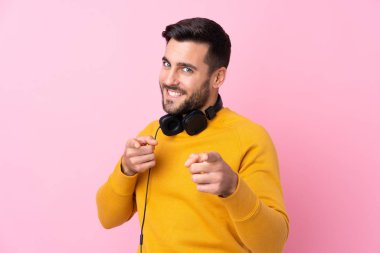 Pembe arka planda kulaklıkları olan genç ve yakışıklı bir adam kendine güvenen bir ifadeyle seni işaret ediyor.