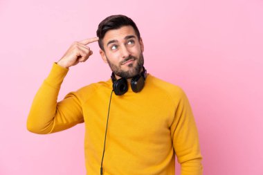 Kulaklık takan, pembe arka planda kuşkuları olan ve kafası karışmış genç, yakışıklı bir adam.