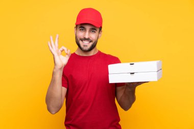 Pizza teslimatçısı üniformalı adam izole edilmiş sarı arka planda pizza kutuları topluyor.