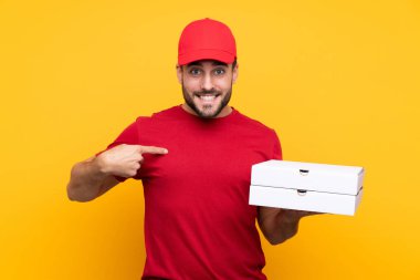 İş üniformalı bir pizzacı, izole edilmiş sarı arka planda pizza kutuları alıyor ve yüzünde sürpriz bir ifade var.