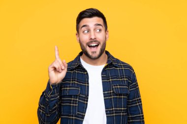 Sarı arka planda sakallı yakışıklı genç adam çözümü bulmak için parmağını kaldırıyor.