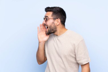 Sakallı, mavi arka planda genç yakışıklı bir adam ağzı açık bağırıyor.