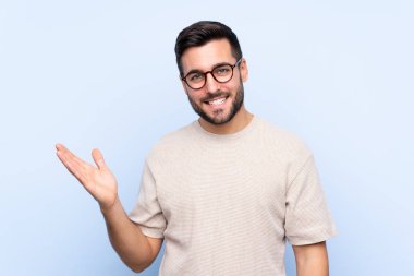 İzole edilmiş mavi arka planda sakallı genç yakışıklı bir adam.