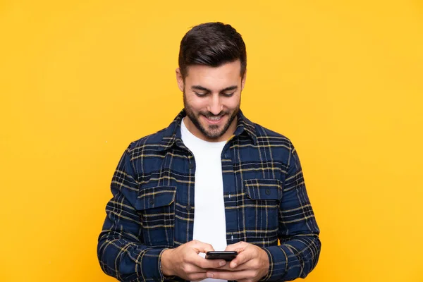 Sarı Arka Planda Sakallı Yakışıklı Genç Adam Cep Telefonuyla Mesaj — Stok fotoğraf