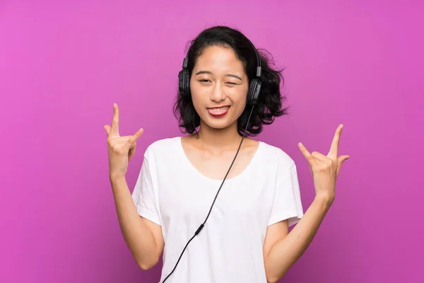 Asiática joven escuchar música con un móvil sobre aislado púrpura pared — Foto de Stock