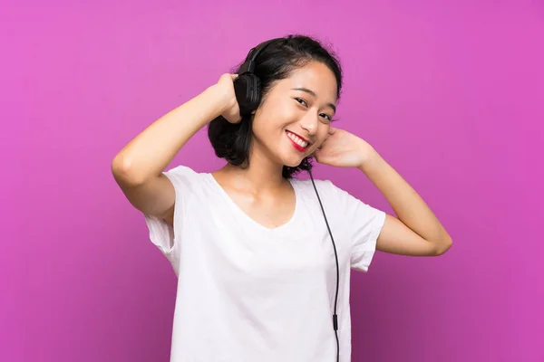 Asiática joven escuchar música con un móvil sobre aislado púrpura pared — Foto de Stock