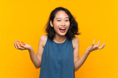 Young asian girl holding a grapefruit over isolated orange background with shocked facial expression