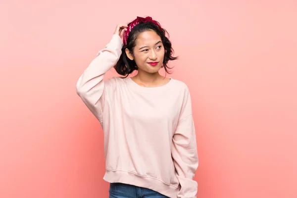 분홍빛 배경을 아시아 소녀가 머리를 긁으면서 의심을 — 스톡 사진