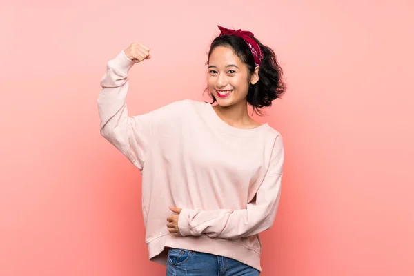亚洲年轻女子在孤零零的粉红背景上做着强有力的手势 — 图库照片