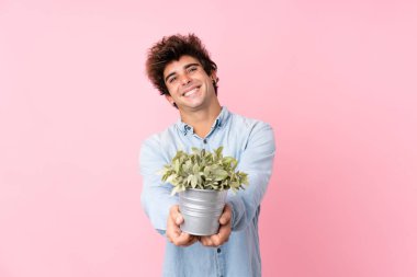 Soyutlanmış pembe arka planda genç beyaz bir adam bir saksı alıyor.
