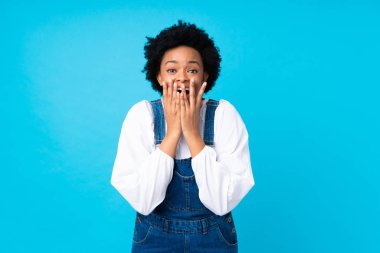 Tulum giymiş, mavi arka planda sürpriz bir yüz ifadesi olan Afro-Amerikalı kadın.