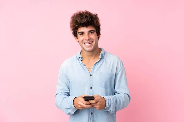 年轻的高加索人男子通过孤立的粉色背景发送消息或电子邮件与手机 — 图库照片