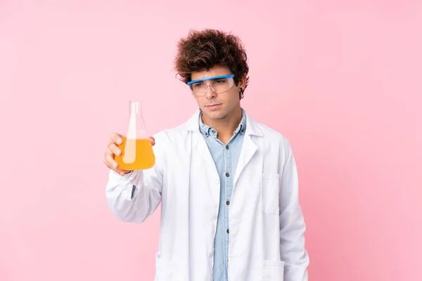 用科学实验管将年轻的高加索人男子置于孤立的粉色背景之上 — 图库照片