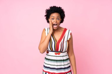Yüzü şoke olmuş ve şaşırmış bir şekilde pembe arka planda kalan Afro-Amerikalı bir kadın.