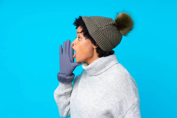 非洲裔美国妇女 头戴冬季帽 在孤立的蓝色背景上大喊大叫 张大嘴 — 图库照片