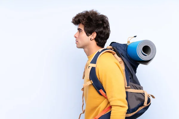 Joven montañero con una gran mochila sobre bac azul aislado —  Fotos de Stock