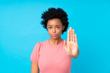 Afrika kökenli Amerikalı bir kadın, mavi arka planda, elleriyle durdurma hareketi yapıyor.