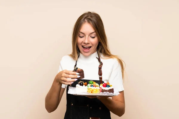 Young Blonde Woman Isolated Background Holding Mini Cakes Surprised — Stock Photo, Image