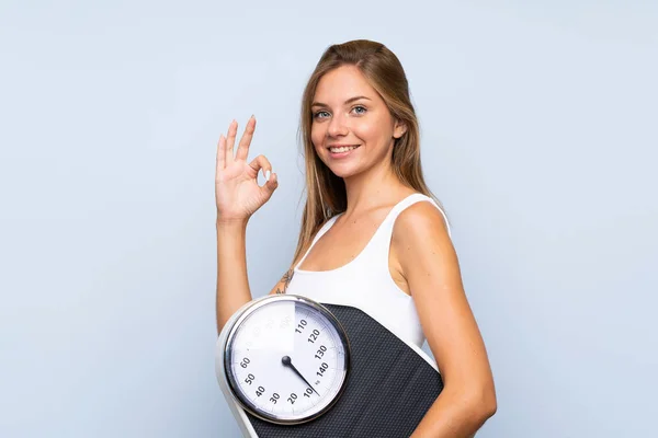 Young blonde girl with weighing machine over isolated blue white — Stock Photo, Image