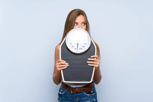 Chica rubia joven con máquina de pesaje sobre aislado azul blanco — Foto de Stock