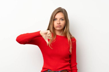 İzole edilmiş beyaz arka planda kırmızı kazaklı genç sarışın kadın baş parmağını aşağı gösteriyor.