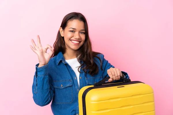 旅行コロンビア人女性保持上のスーツケース隔離されたピンクの背景ショーOk Signとともに指 — ストック写真