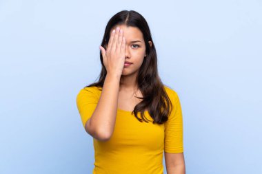 İzole edilmiş mavi geçmişi olan genç bir Kolombiyalı kız, bir gözü elle kapatıyor.