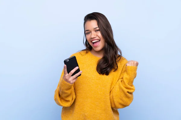 Jong Colombiaans Meisje Met Trui Geïsoleerde Blauwe Achtergrond Met Telefoon — Stockfoto