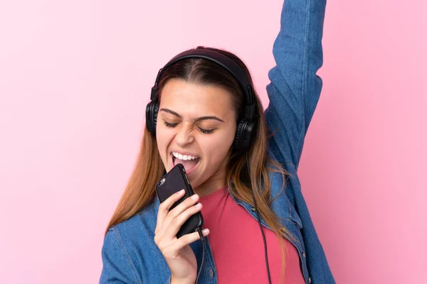 Teenager κορίτσι ακούγοντας μουσική με ένα κινητό πάνω από απομονωμένο ροζ w — Φωτογραφία Αρχείου