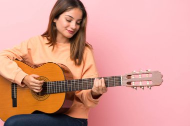 İzole edilmiş pembe arka planda gitar çalan esmer bir kız.