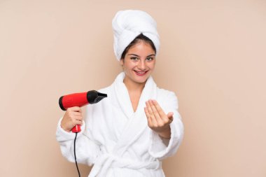 Saç kurutma makineli bornozlu genç bir kadın izole bir arka planda, bizimle gelmek için davet ediyor. Gelmene sevindim.