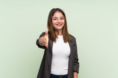 Yeşil arka planda ceketi olan esmer genç kız iyi bir anlaşma için el sıkışıyor.